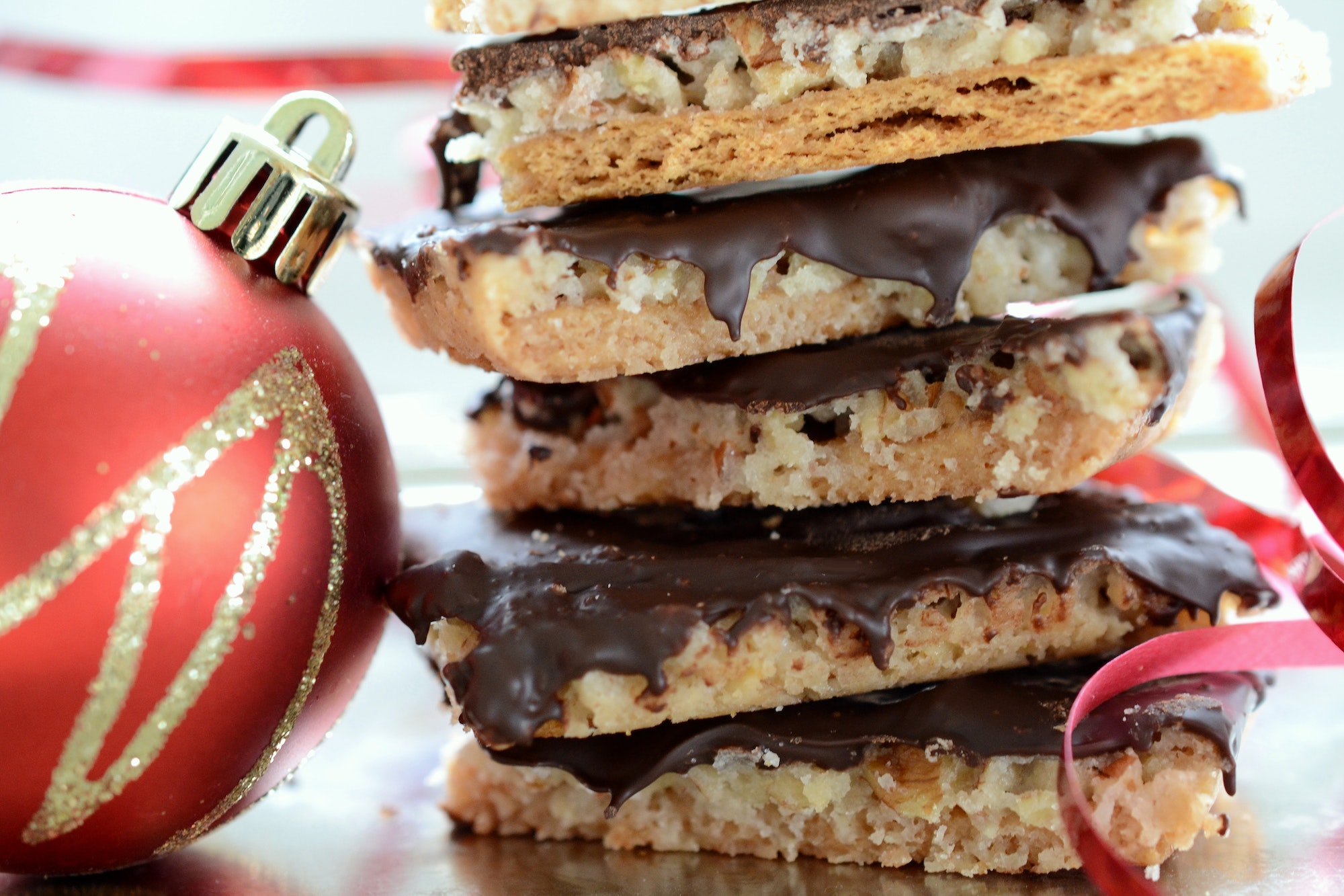 A stack of homemade Christmas treats cookies next to a red gold Christmas ornament red curly ribbon