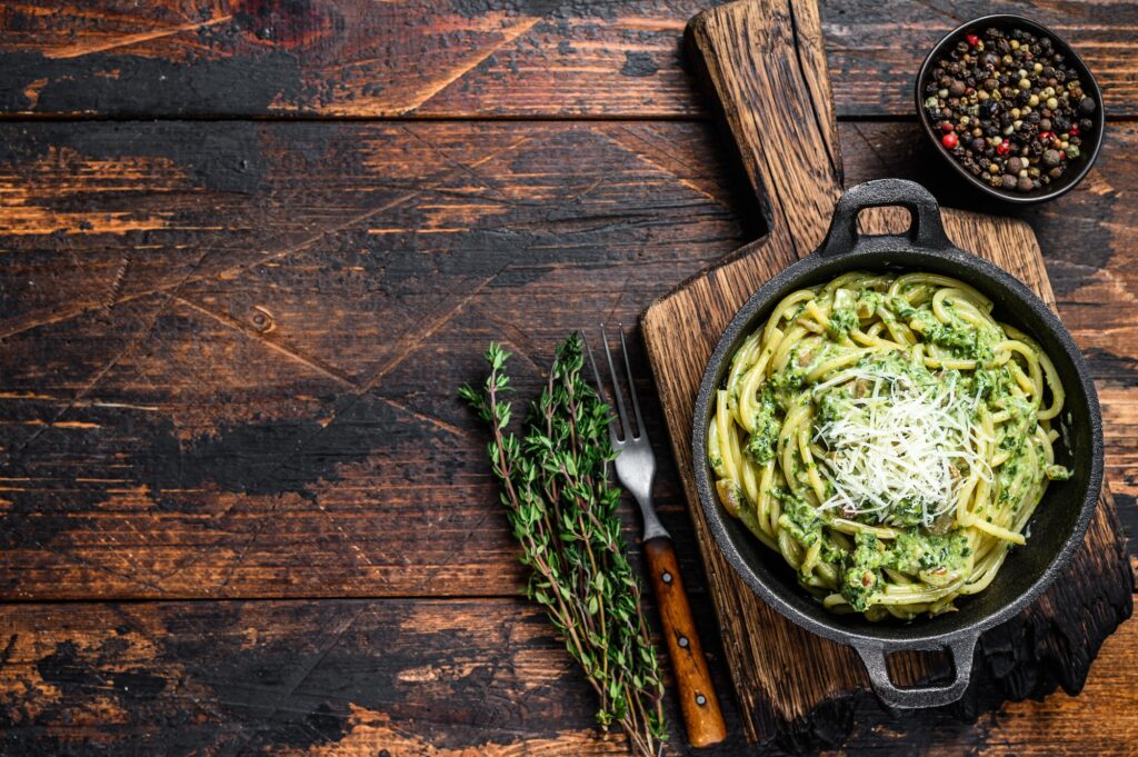 Spaghetti Pasta with pesto sauce, spinach and parmesan in a pan. Dark Wooden background.