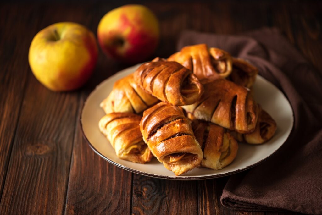 Homemade rolls buns with apples and cinnamon on brown wooden background